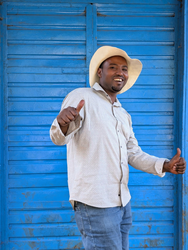 Man wearing a white shirt and hat standing in front of a blue shutter
