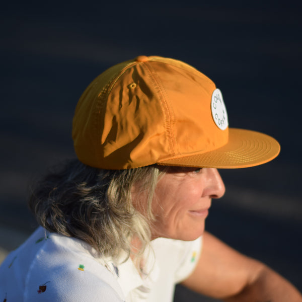 Color Coffee nylon gold cap on side profile of a woman sitting down