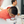 Load image into Gallery viewer, A man in a coral orange polo shirt and glasses leans over a table filled with small white cups, with another man blurred in the background.
