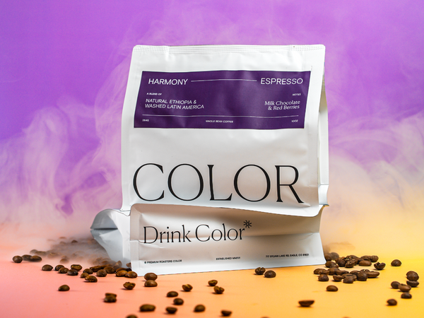 A stand-up pouch of Color Drink Color espresso coffee beans on a stylized purple-to-orange gradient background with coffee beans scattered around the base. The front label reads 'HARMONY' and 'ESPRESSO'.
