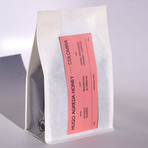 Colombia Hugo coffee in 10oz white whole bean coffee bag with pink label with coffee details on it