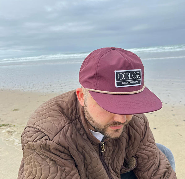Man with a brown coat wearing an Eggplant 5 panel nylon hat