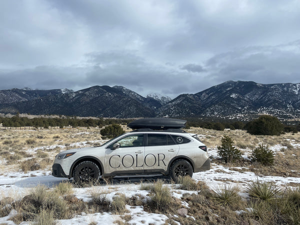 Car with 'COLOR' branding parked in a snowy landscape with mountains in the background