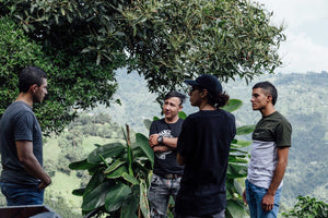 Four men standing outdoors with a scenic background of trees and mountains.