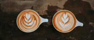 two white mugs on brown background with beautiful latte art - photo by Nathan Dumlao