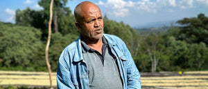 whole bean coffee farmer standing with drying racks behind him in Ethiopia