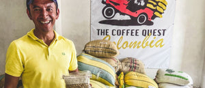 Male coffee producer in yellow polo shirt with stacked coffee burlap sacks in the background