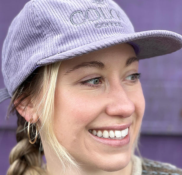 close up of a blonde hair woman with a purple corduroy hat
